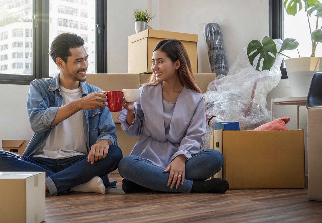 Two people sitting on the floor of their new apartment, drinking coffee with boxes surrounding them as they unpack.