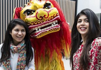 Two women smiling with a colorful lion dance costume head in the background, symbolizing Lunar New Year celebrations.