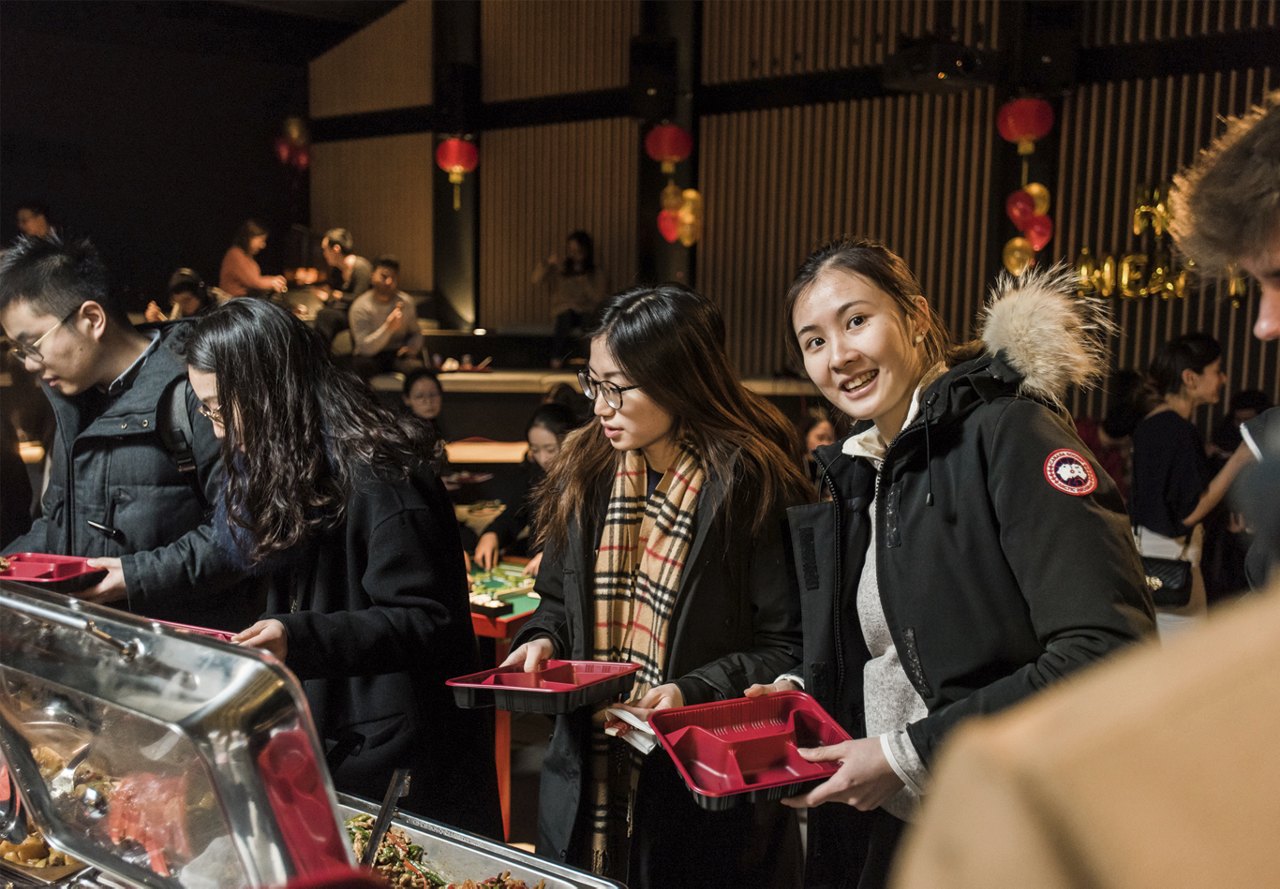 People lining up at a buffet with traditional decorations, during a Lunar New Year event.