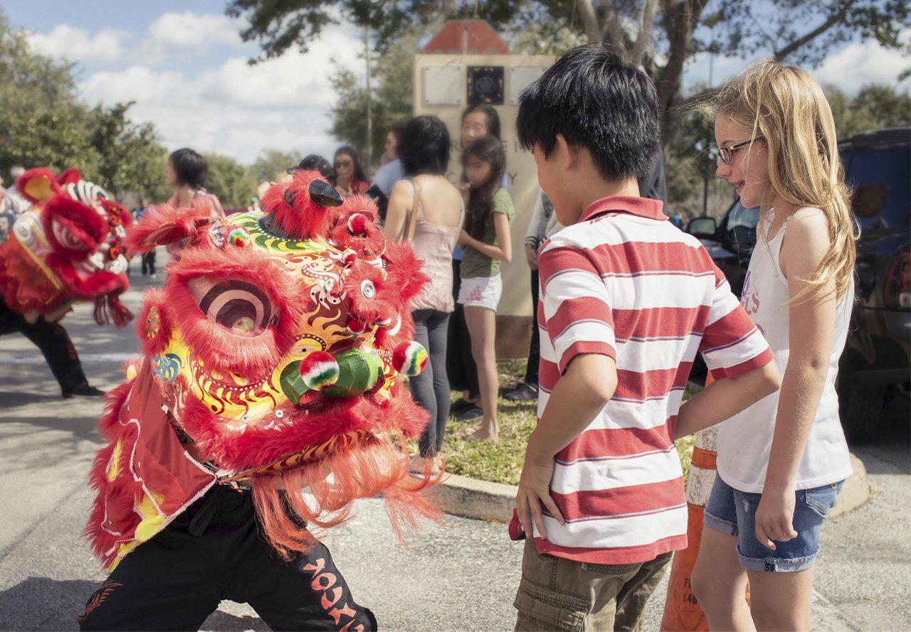 Children watching a lion dance performance in an outdoor community event.