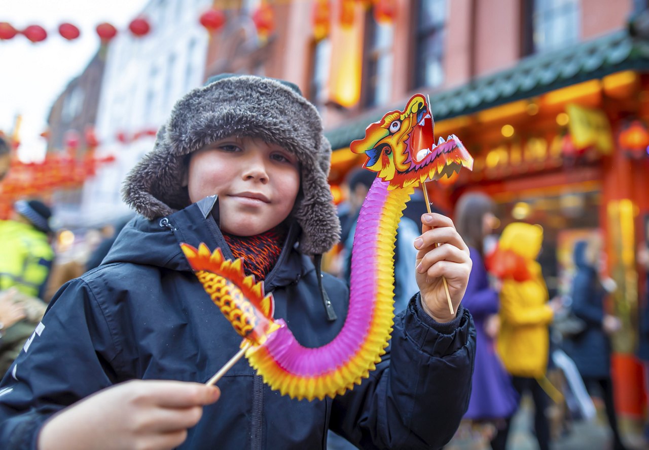 A boy in winter clothing holds a colorful dragon puppet at a Lunar New Year street celebration.