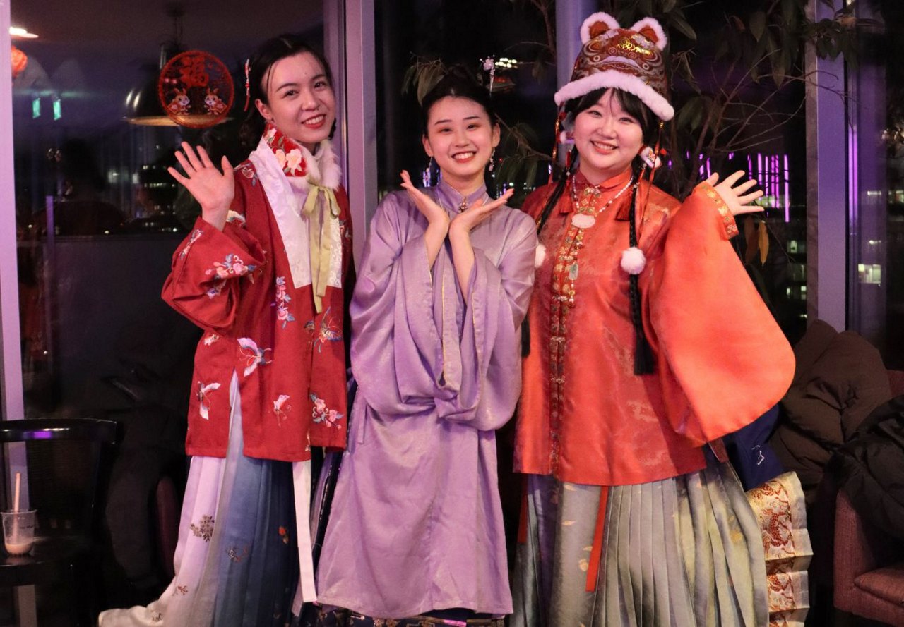 Three women in traditional Asian attire smiling and posing during Lunar New Year festivities.