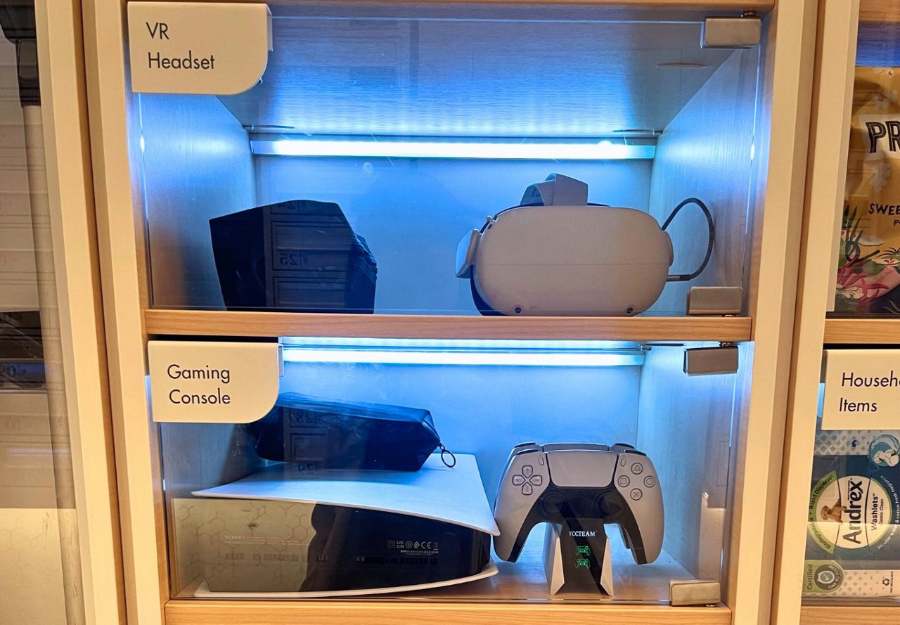 Glass cabinet shelves displaying a VR headset and a gaming console with a controller, labeled respectively for rental.