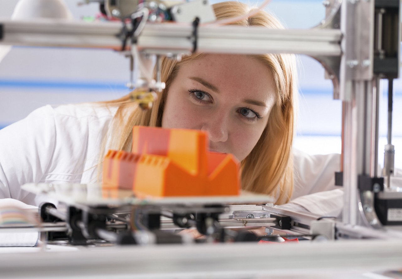 Focused engineer examining a 3D printed orange model with precision on a 3D printer in a laboratory setting.