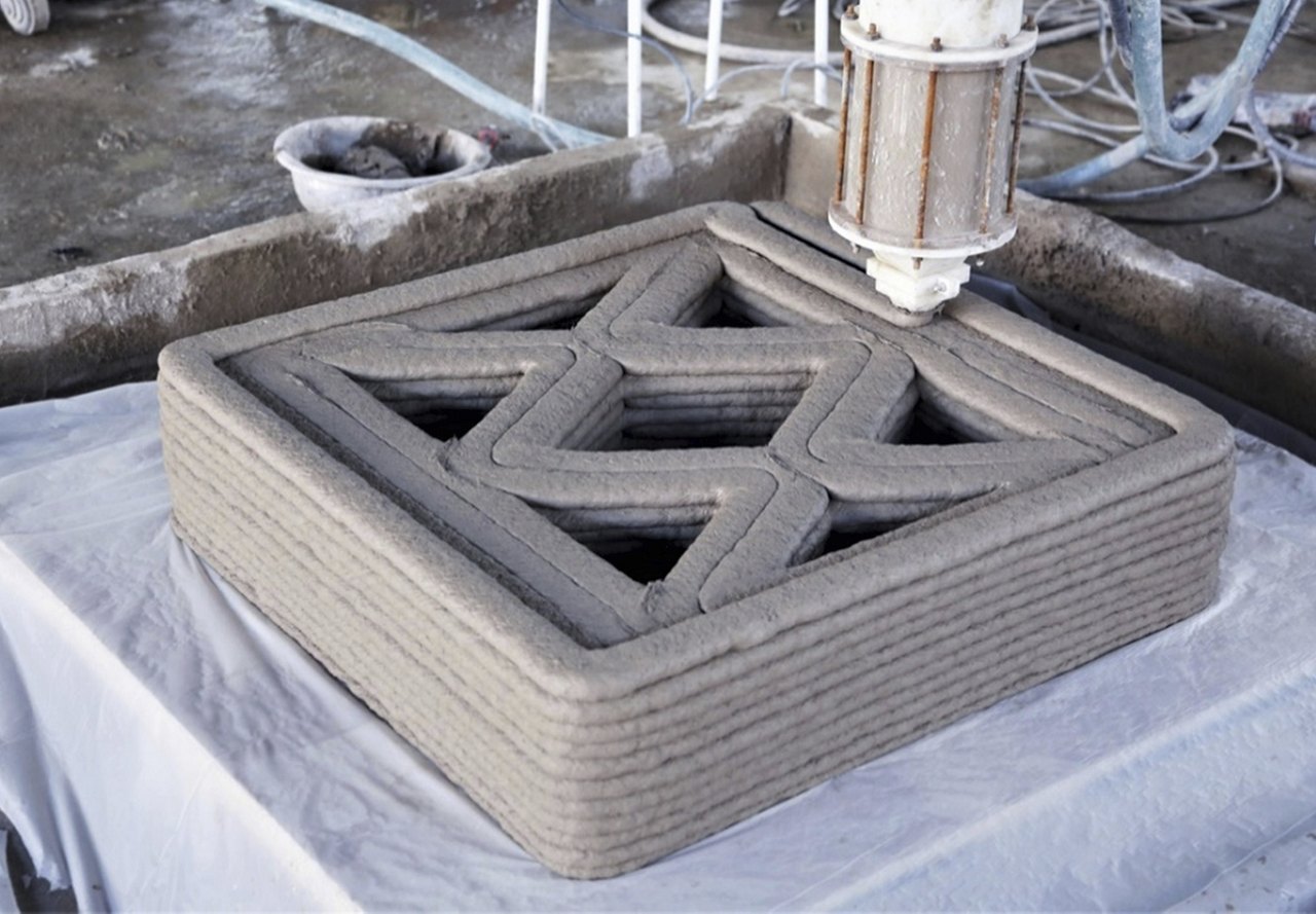 A robotic arm 3D printing a concrete structure in a star-shaped layer pattern at a construction site.
