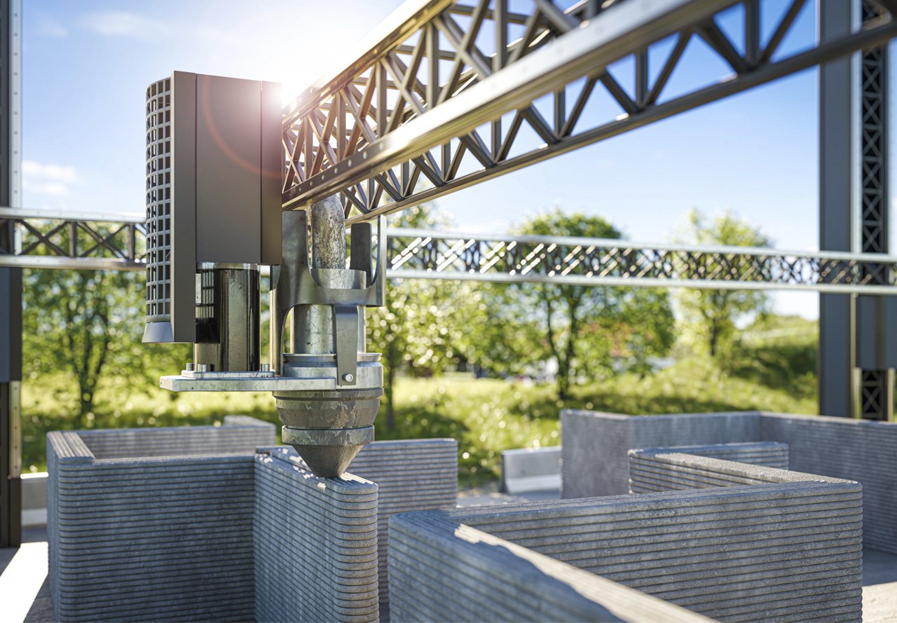 Close-up of a 3D printer constructing layered concrete walls in an outdoor setting with greenery in the background.