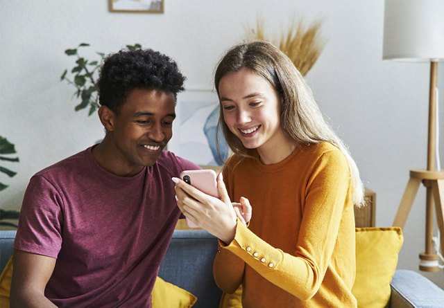 Two friends sharing a moment of joy while looking at a smartphone in a cozy living room.