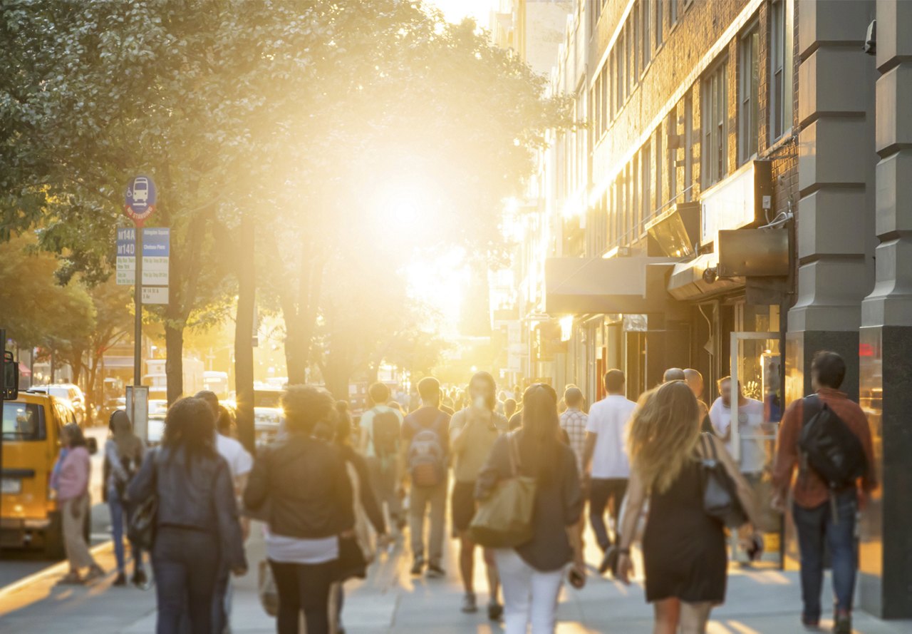 People walking down the sidewalk in a busy city with the sun rising