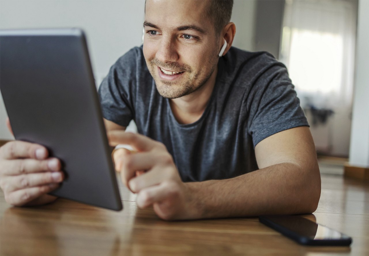 Man smiling while browsing on tablet with wireless headphones in