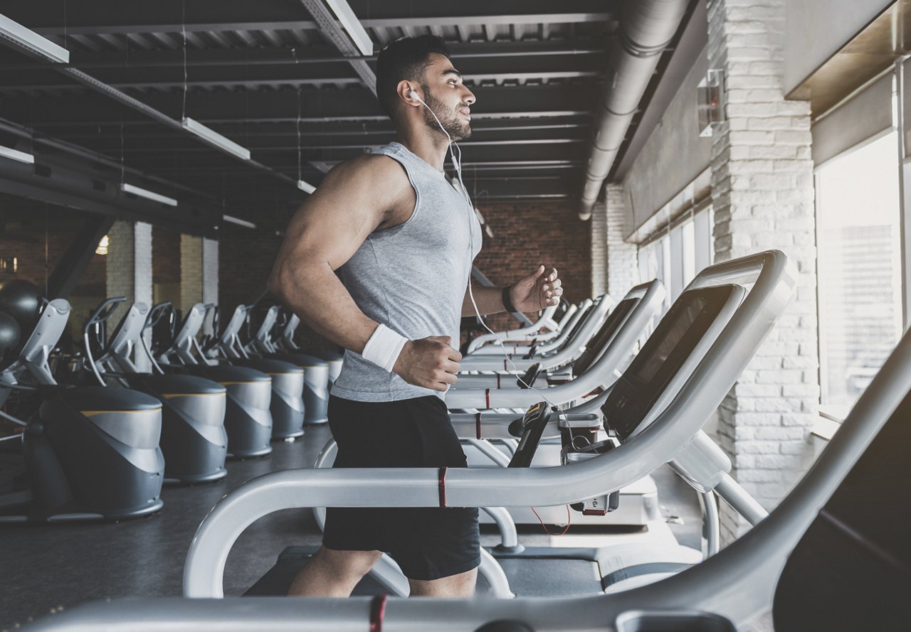 Man running on treadmill at his apartment gym surrounded by other workout equipment 