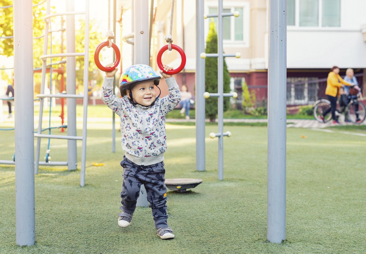 Small child with helmet on playing in the play area at an apartment complex