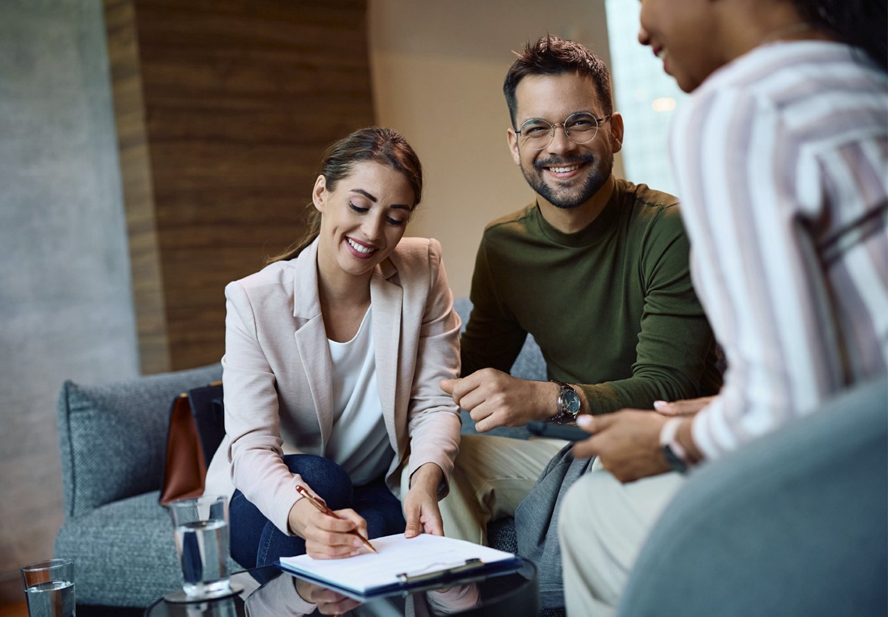 Couple signing lease document and smiling while sitting with another woman