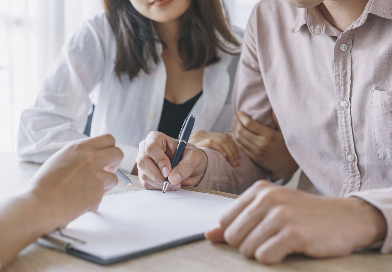 Couple sitting down at table and signing paperwork with black pen