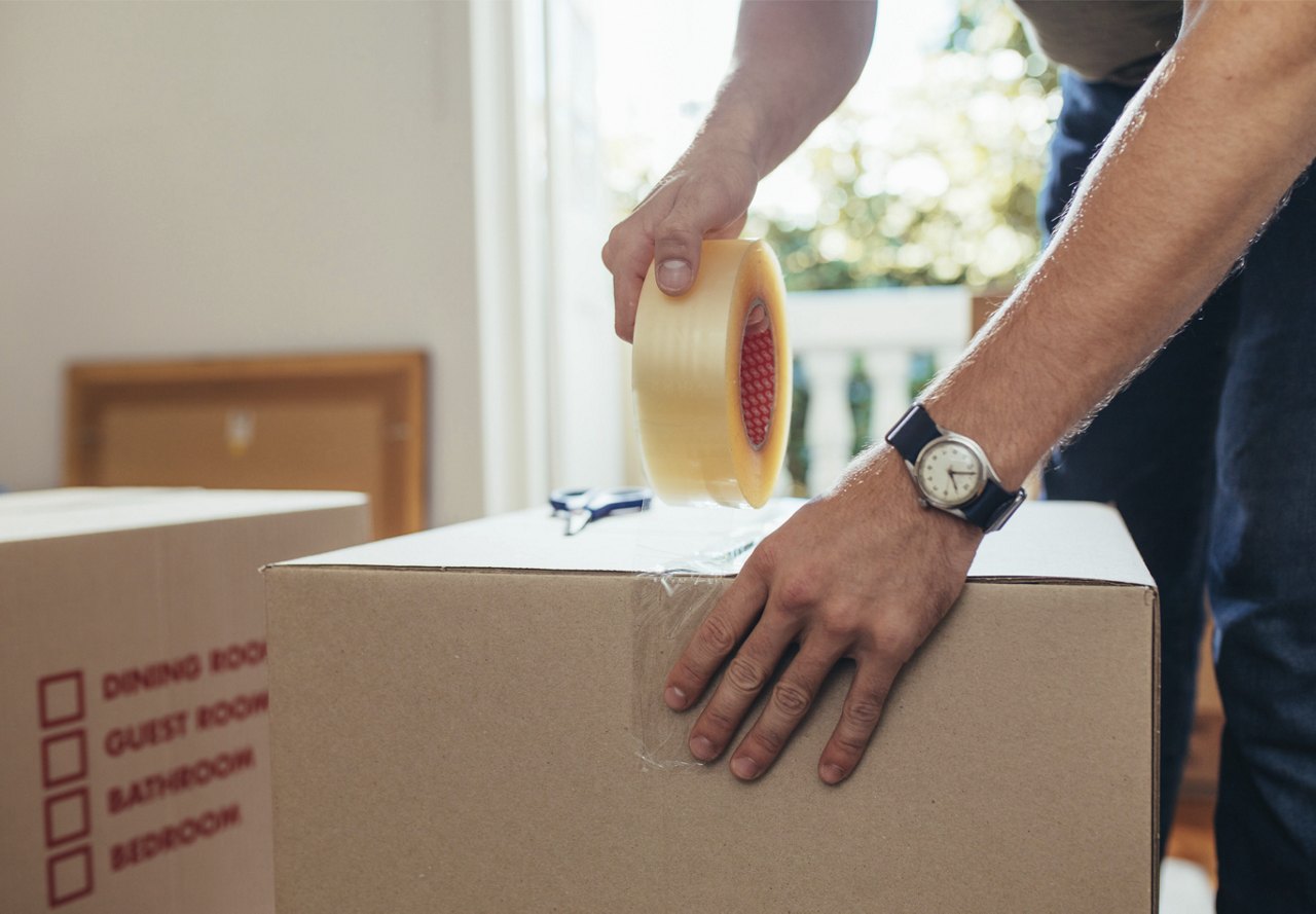 Man using roll of tape to secure cardboard boxes when preparing for a move