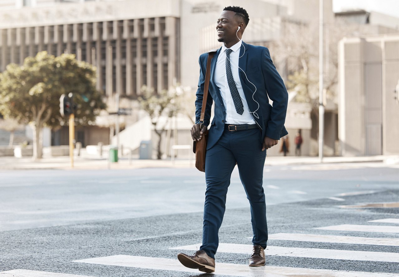 African American man walking across the street with business suit on and headphones