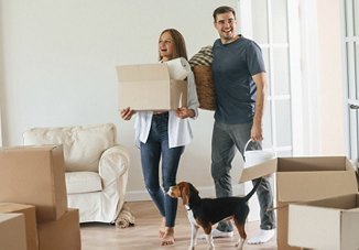 Young couple walking into new apartment for the first time with their dog holding boxes