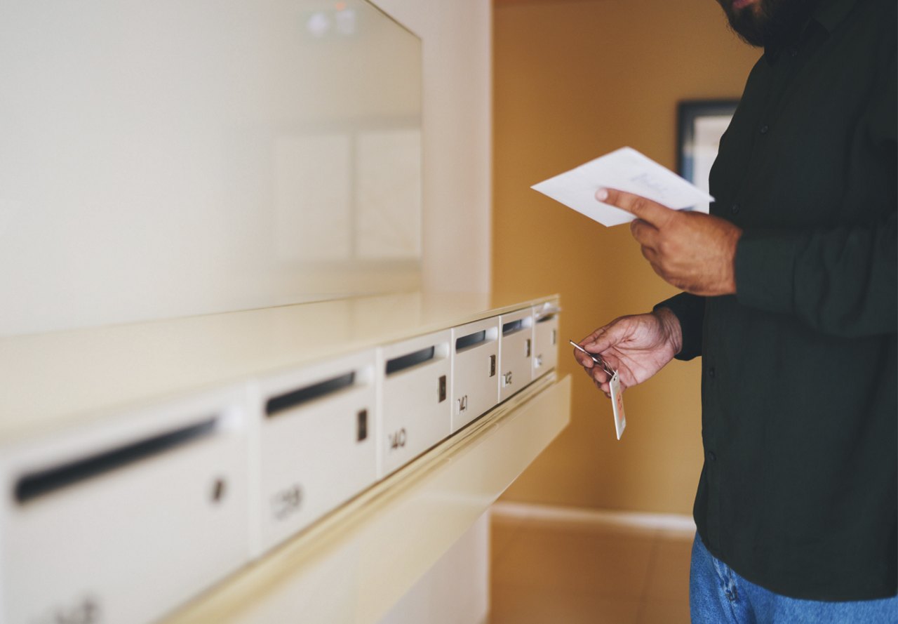 Man opening mailbox with key at apartment building and holding white envelope