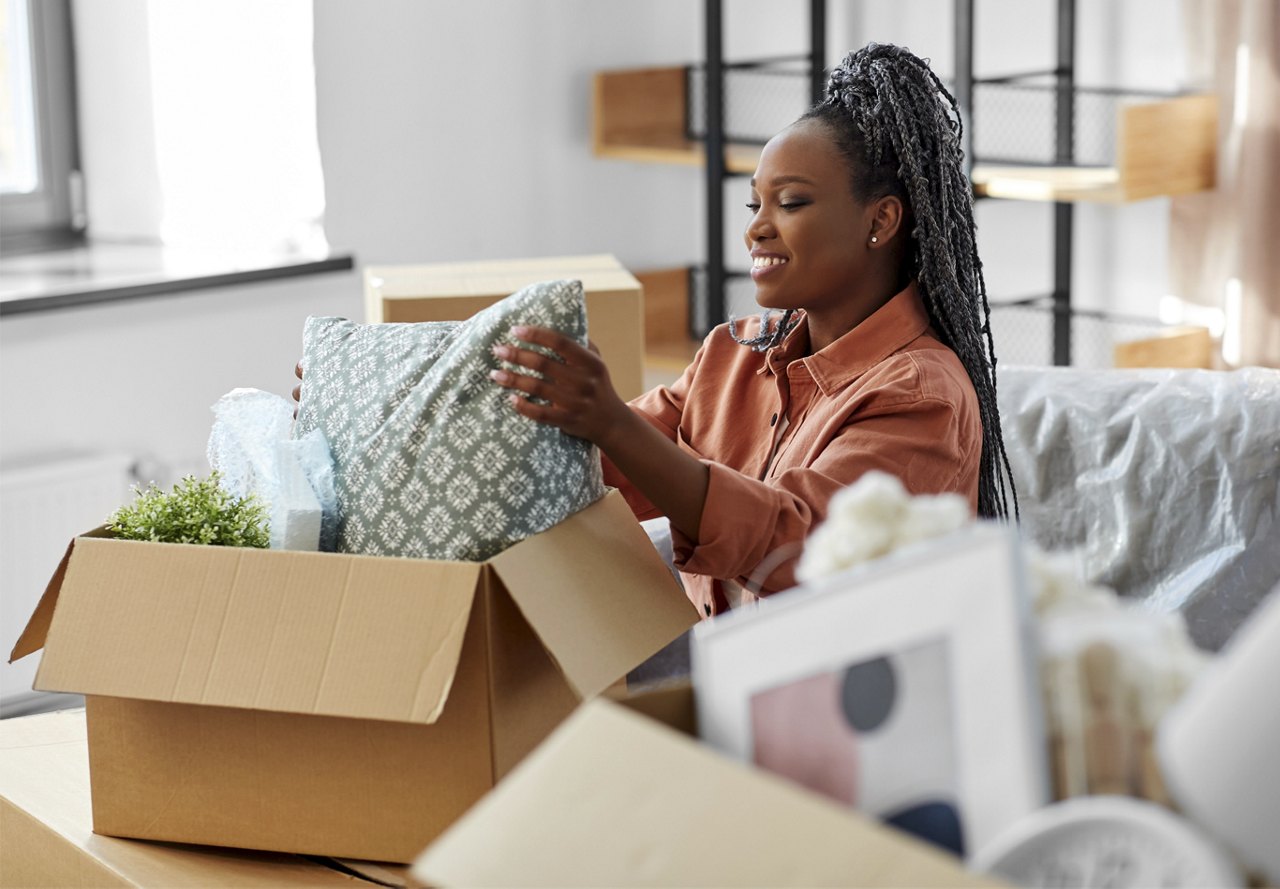 Young African American woman unpacking boxes with decor for her apartment