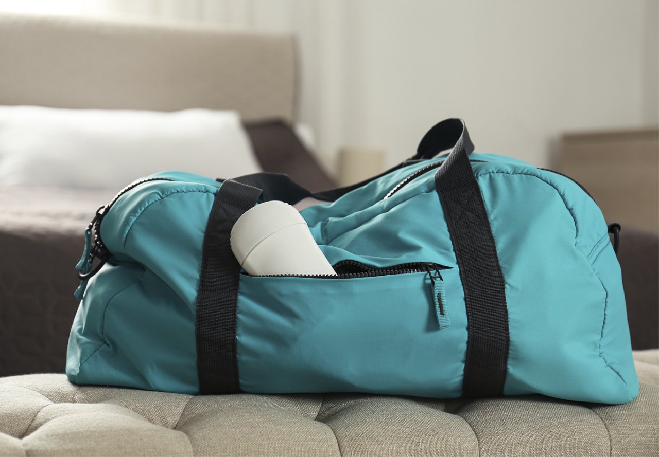 A teal gym bag with a white water bottle poking out, resting on a bench in a home environment.