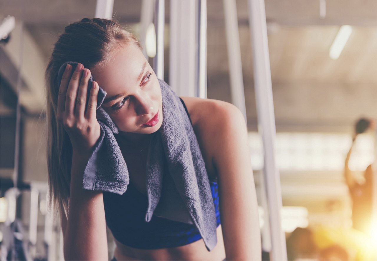 A woman resting with a towel over her shoulders, wiping sweat from her forehead after a workout.