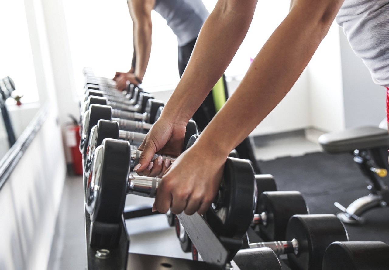 Close-up of hands selecting dumbbells from a weight rack in a gym.