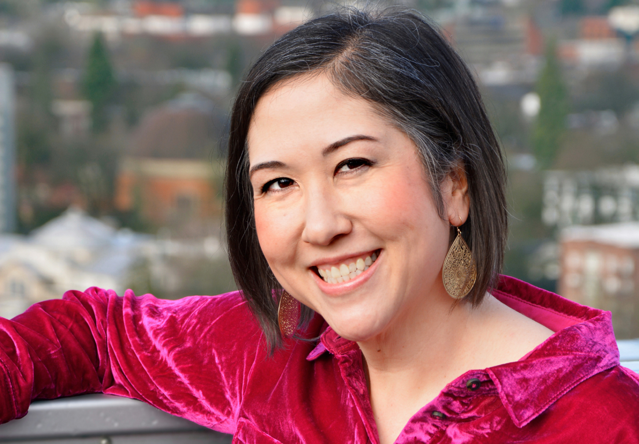 Smiling woman in a vibrant red velvet top with urban scenery in the background.
