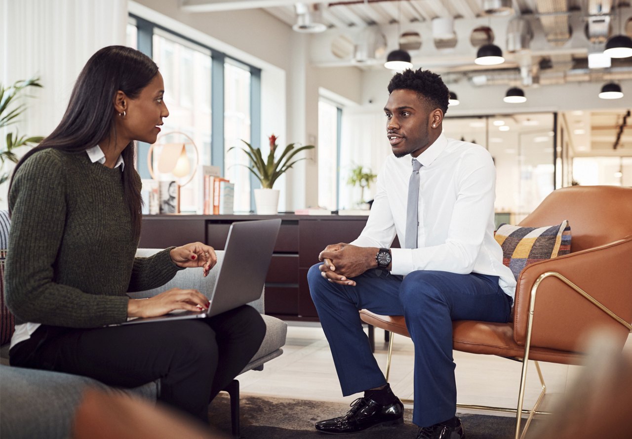 young man speaking to woman with computer in sitting area for an interview