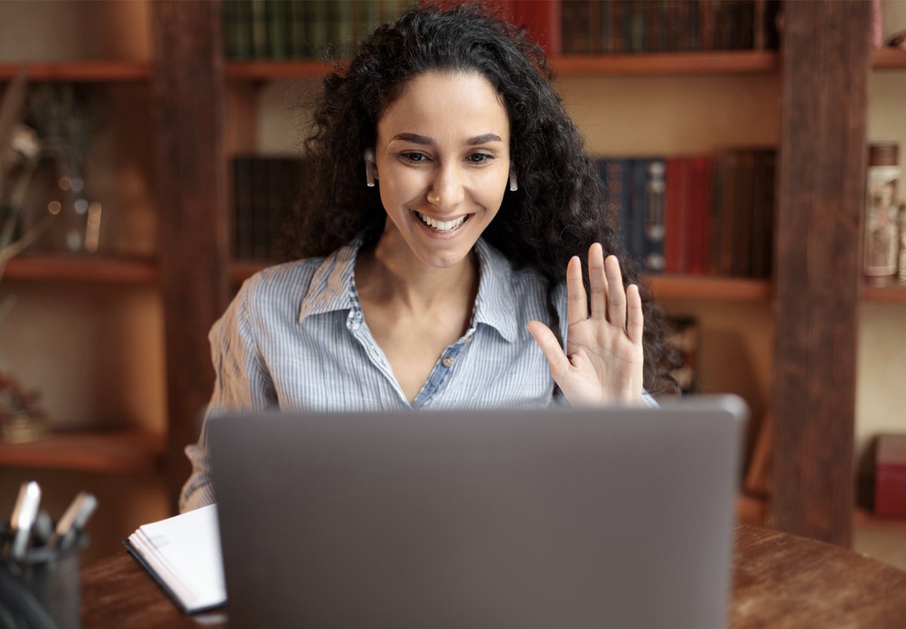 young woman waving at the end of virtual interview on laptop in office