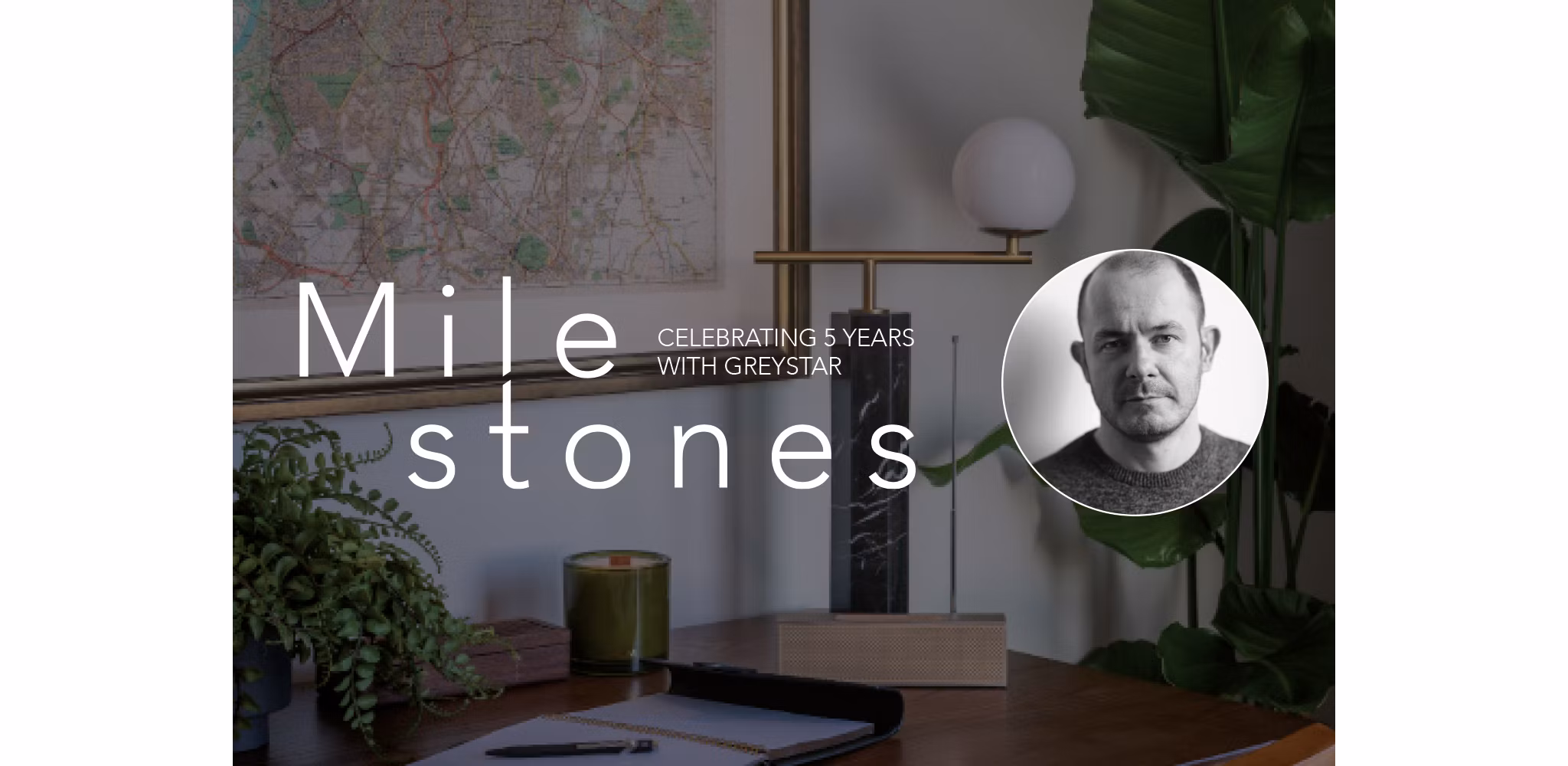 Office desk with decor, featuring the text 'Milestones, Celebrating 5 Years with Greystar' next to a portrait of a man.