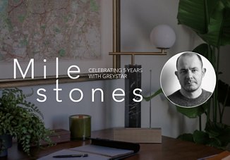 Office desk with decor, featuring the text 'Milestones, Celebrating 5 Years with Greystar' next to a portrait of a man.