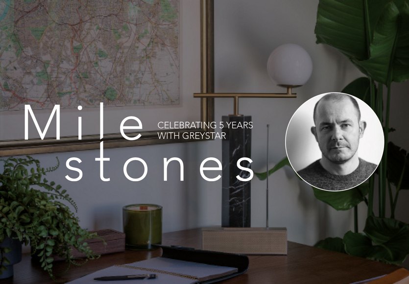 Office desk with decor, featuring the text 'Milestones, Celebrating 5 Years with Greystar' next to a portrait of a man.