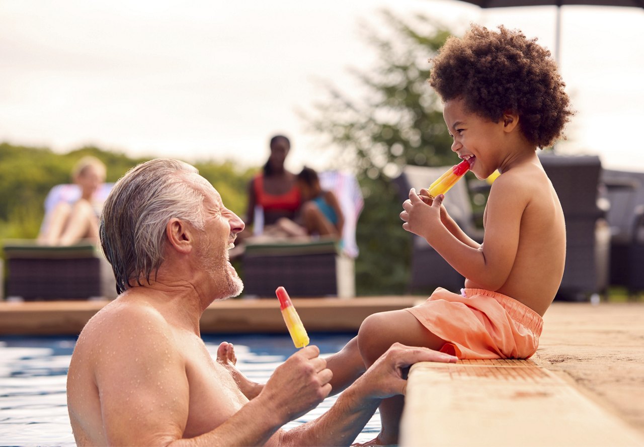 An older man and a child enjoying popsicles by the pool.