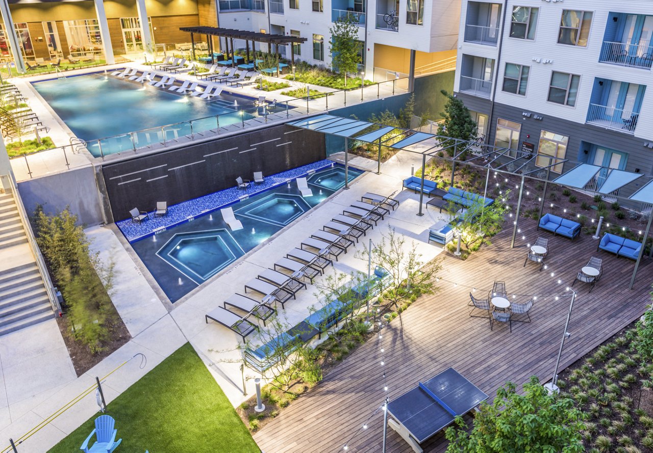 Aerial view of an apartment complex pool area with lounge chairs and seating areas.