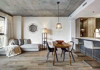 A modern apartment living area featuring a dining table, couch, and bar with an industrial design, illuminated by bright, ambient lighting to create a vibrant and stylish atmosphere.