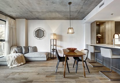 A modern apartment living area featuring a dining table, couch, and bar with an industrial design, illuminated by bright, ambient lighting to create a vibrant and stylish atmosphere.