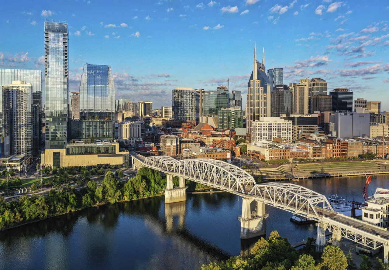 Cityscape of Nashville, Tennessee, featuring a bridge spanning over the water, with a vibrant blue sky overhead, showcasing the city's scenic beauty.