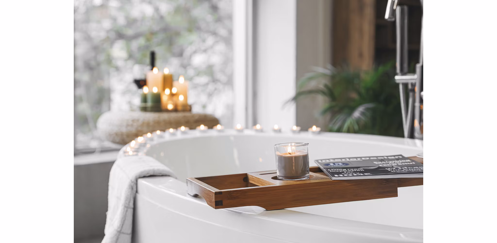 Luxurious bathroom featuring a bathtub surrounded by candles, a tray holding a magazine, and abundant natural light, creating a serene and spa-like atmosphere in a modern apartment.