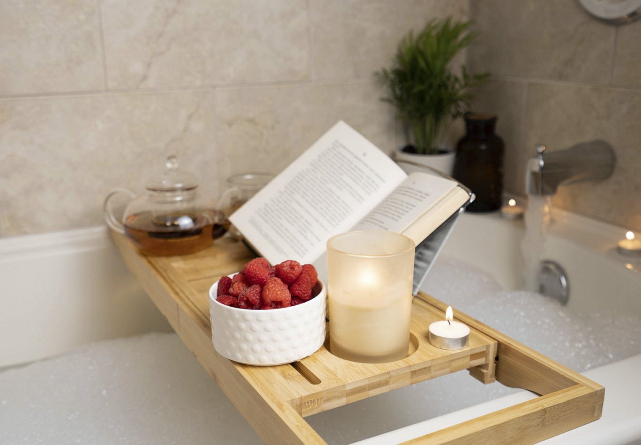 Bubble bath with a bathtub tray holding a book, candle, tea, and fresh berries, set against neutral tiles and décor, creating a serene and relaxing atmosphere for unwinding.