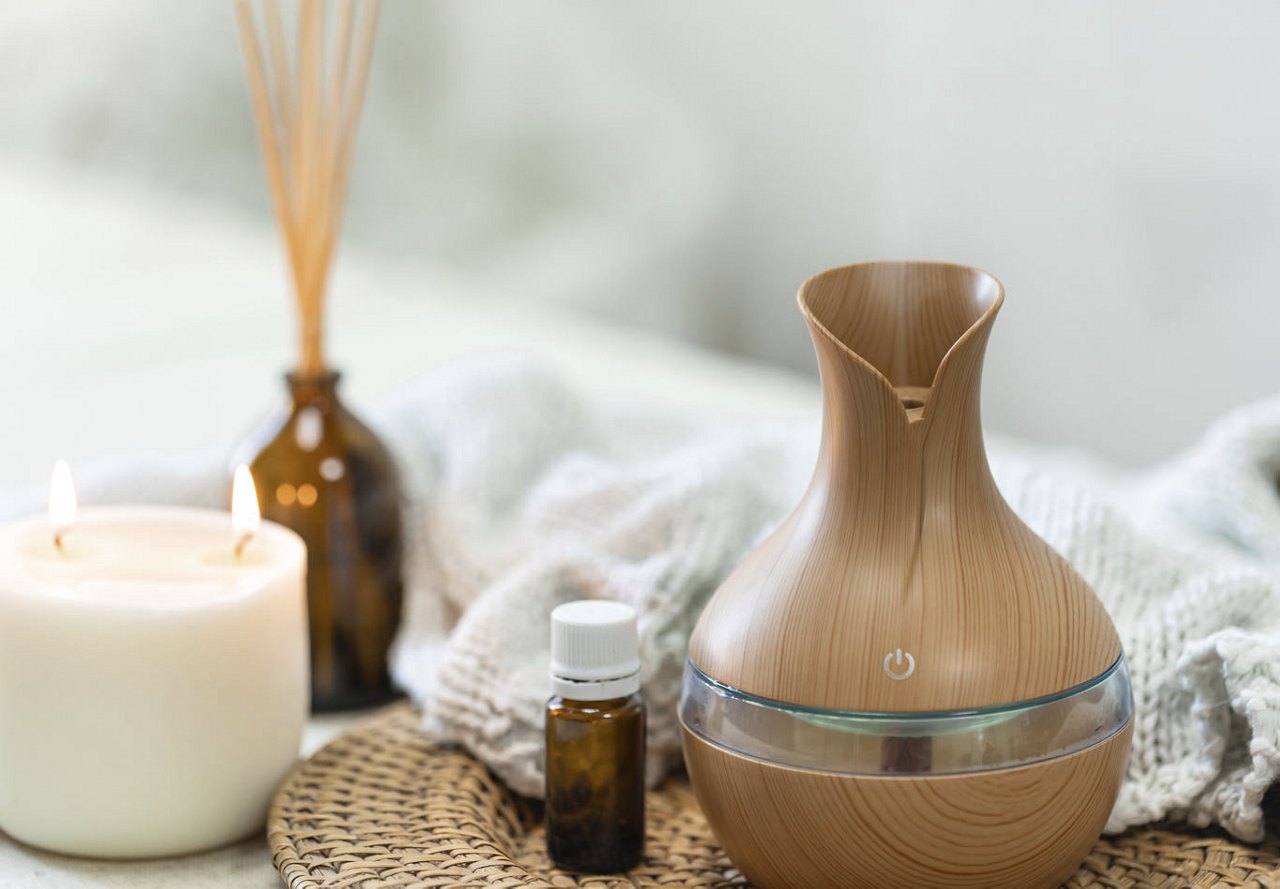 Wooden oil diffuser in a serene bathroom setting, accompanied by a candle and essential oils, creating a warm and relaxing atmosphere with thoughtfully arranged spa essentials.