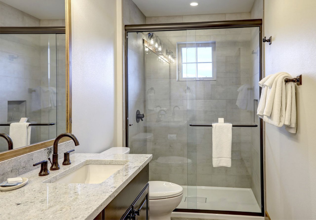 Walk-in shower with neutral tile in a modern bathroom, featuring white towels on a towel holder and neutral granite countertops, creating an upscale, spa-like atmosphere.