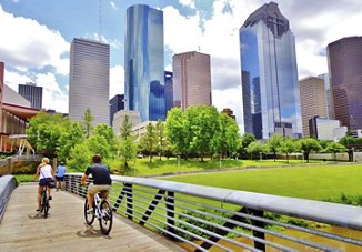 Residents in Houston, Texas, riding their bikes together in a park, surrounded by lush greenery and enjoying a beautiful day, with the city skyline visible in the background.