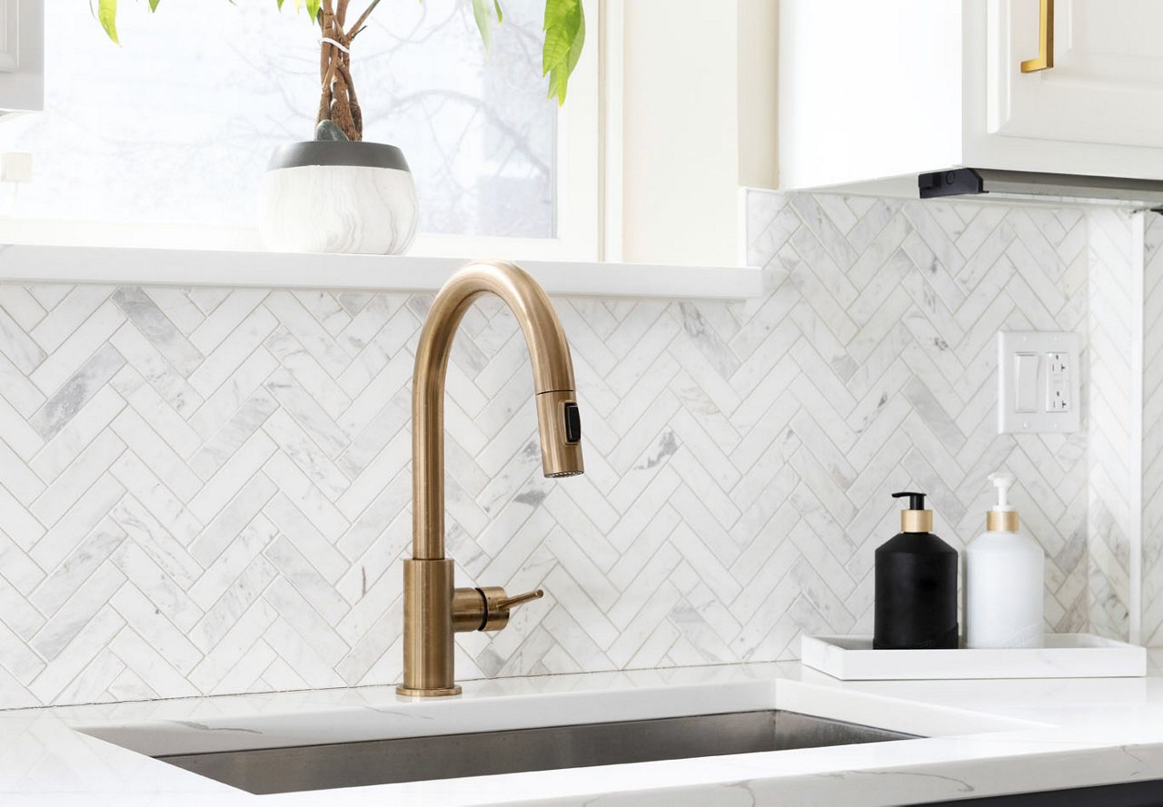 Modern kitchen counter featuring a geometric backsplash and sleek gold hardware, with a large window behind it bringing in natural light. A potted plant adds a touch of greenery to the space.