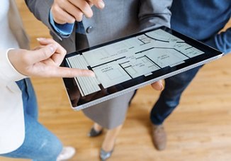 People pointing at a floorplan on a tablet while standing together in an apartment unit after a tour, discussing the layout in more detail.