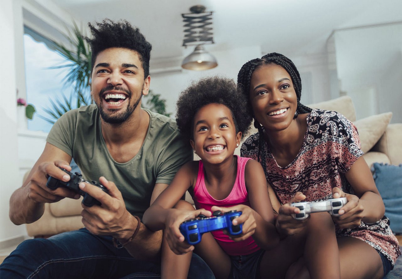 A family sitting together on the couch, smiling and enjoying their time playing video games while looking at the TV screen.