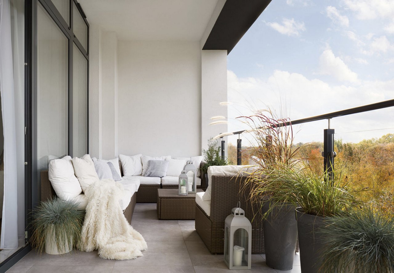 A modern outdoor balcony of an apartment featuring stylish decor, a cozy couch with a blanket, and overlooking stunning natural scenery, creating a peaceful and inviting space.