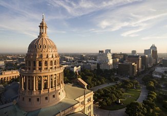 A view of downtown Austin, Texas, featuring the Texas State Capitol as the focal point, with the city skyline and dramatic clouds in the background.