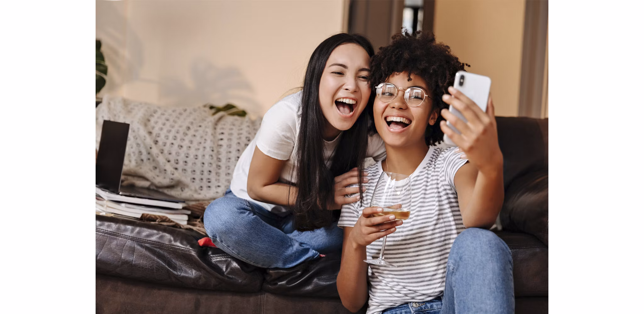 Two roommates smiling as they take a selfie in their cozy living area, enjoying glasses of wine and capturing the joyful moment in their home.