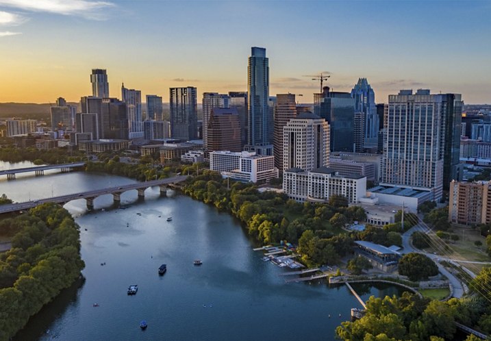 A stunning Texas city skyline reflected in a nearby body of water, set against a vibrant blue and orange sunset.