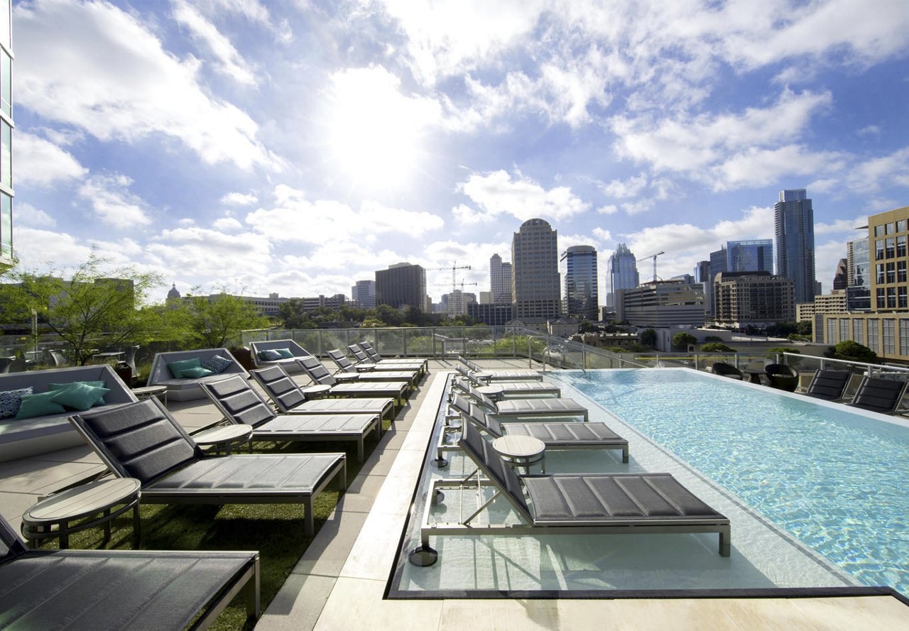 A stunning rooftop pool in Texas with a sparkling blue surface, surrounded by comfortable seating areas, offering residents a picturesque view of the city skyline.