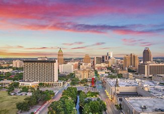 Stunning view of the San Antonio city skyline at sunset, with vibrant pink and purple hues filling the sky above the skyscrapers.